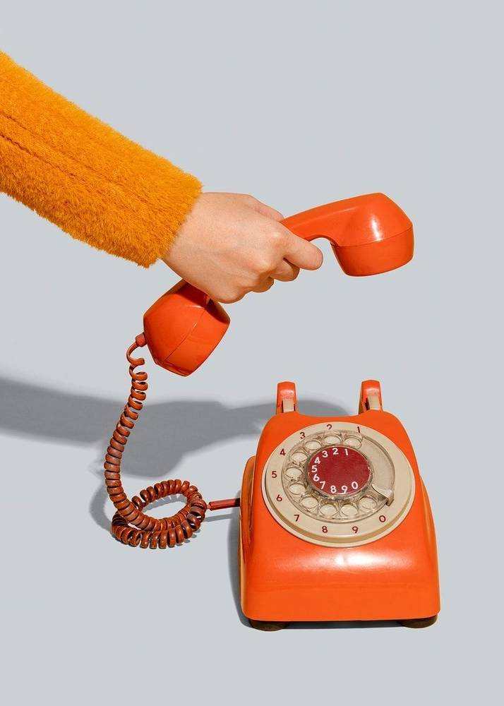 Hand lifting the receiver of an orange telephone